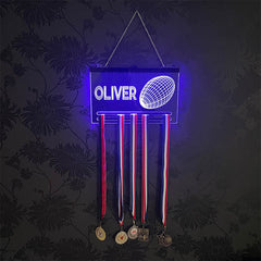 Close-up of a glowing acrylic rugby medal hanger with a name engraved at the top and a detailed rugby ball design, showcasing vibrant blue LED lighting