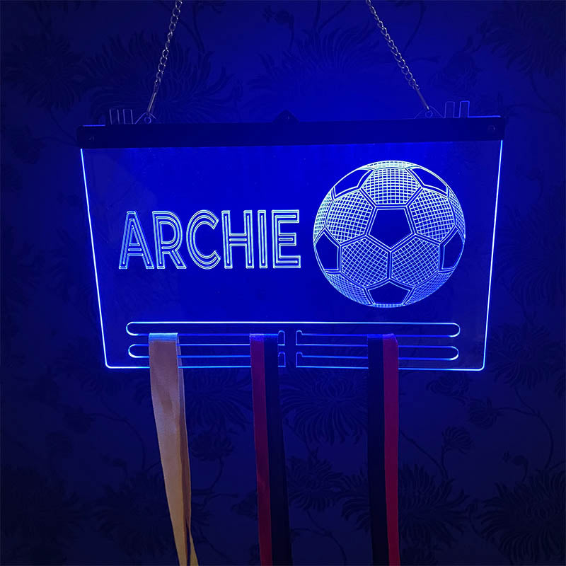 Close-up of a glowing acrylic football medal display with a football graphic and custom engraving, showcasing bright blue LED lighting against a dark background