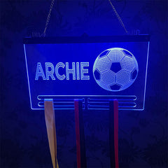 Close-up of a glowing acrylic football medal display with a football graphic and custom engraving, showcasing bright blue LED lighting against a dark background