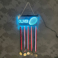 Close-up of a glowing acrylic rugby medal hanger with a name engraved at the top and a detailed rugby ball design, showcasing vibrant blue LED lighting