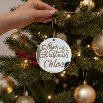 Personalised silver mirror Christmas bauble with “Merry Christmas Chloe” hanging on a decorated tree